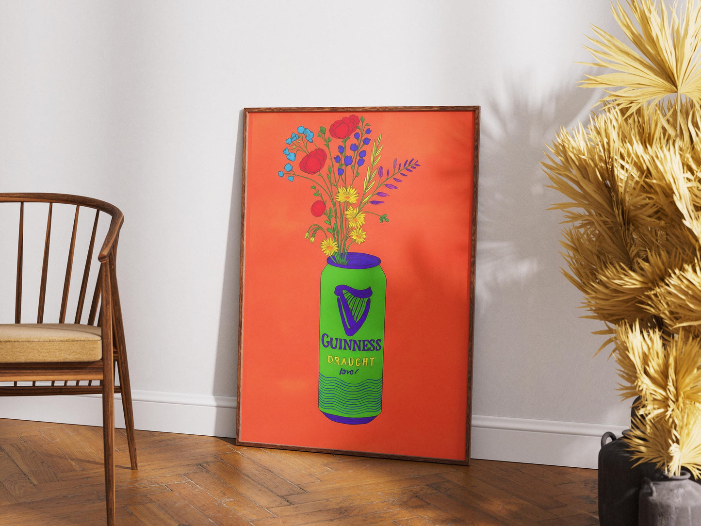 Framed artwork of a Guinness bottle with flowers on an orange background, leaning against a white wall.
