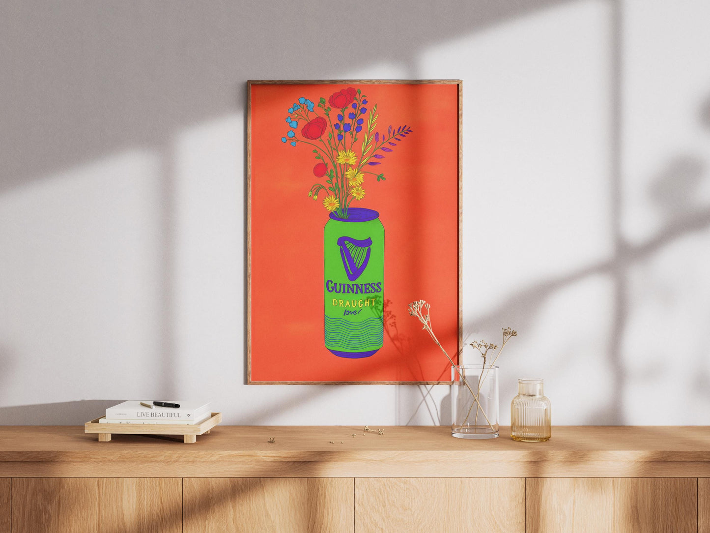 Framed artwork of a Guinness beer bottle with flowers on an orange background, displayed on a wooden surface.