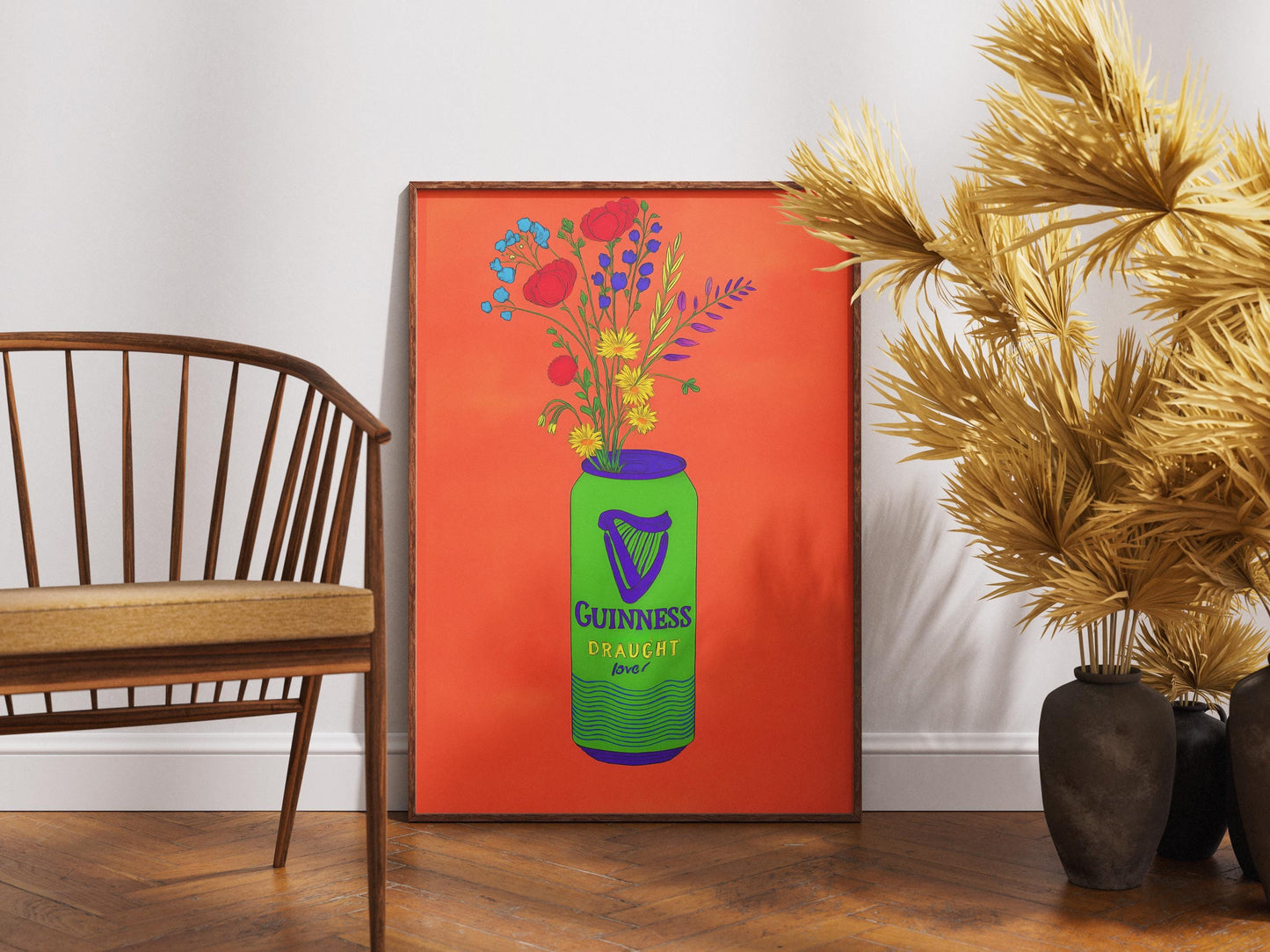 Framed artwork of a Guiness bottle with flowers on an orange background, placed in a room with a wooden chair and decorative plants.