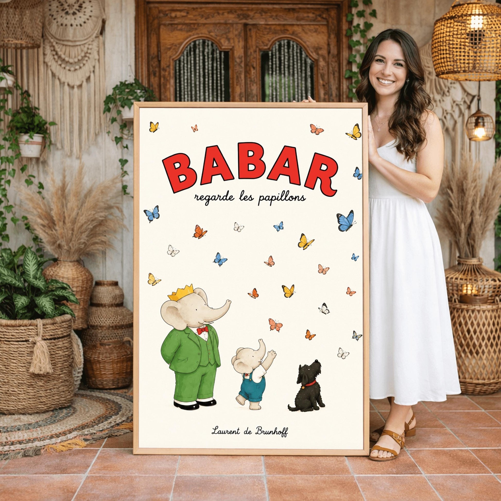 A vertical retro fine art exhibition poster titled "BABAR regarde les papillons" on a wide cream border. The top "BABAR" text is printed in a bold red font. The illustration shows an elephant wearing a crown and green suit standing next to a smaller elephant reaching up toward a sky filled with dozens of colorful blue, yellow, orange, and white butterflies. A small black dog sits patiently on the ground looking up at them. The name "Laurent de Brunhoff" anchors the bottom.