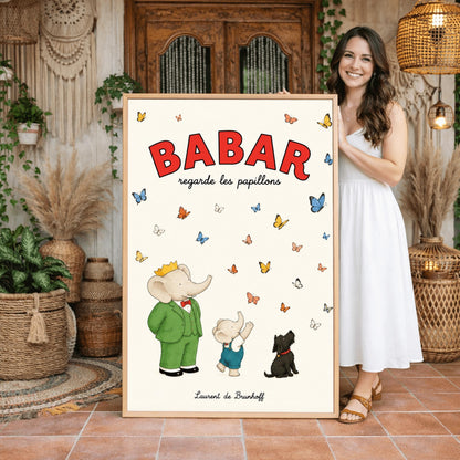 A vertical retro fine art exhibition poster titled "BABAR regarde les papillons" on a wide cream border. The top "BABAR" text is printed in a bold red font. The illustration shows an elephant wearing a crown and green suit standing next to a smaller elephant reaching up toward a sky filled with dozens of colorful blue, yellow, orange, and white butterflies. A small black dog sits patiently on the ground looking up at them. The name "Laurent de Brunhoff" anchors the bottom.