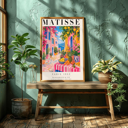 A vertical maximalist art print styled as a Henri Matisse exhibition poster. The scene depicts a vibrant, colorful street in a Mediterranean coastal town. In the foreground, a table with a pink and white striped cloth is piled high with lemons, oranges, and a pineapple. Hot pink and yellow buildings with blue shutters line a cobblestone path that leads toward a blue sea under a bright sky. Lush green trees with yellow lemons and pink flowers frame the view.