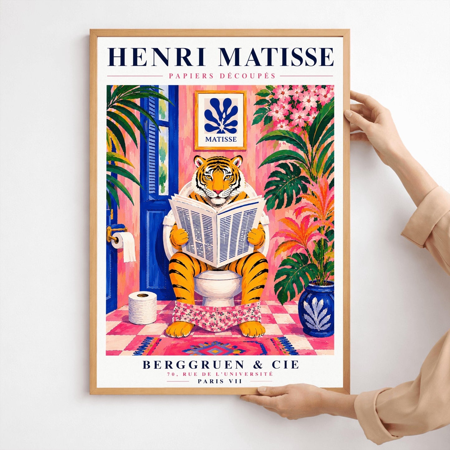 A vertical art print styled as a Henri Matisse exhibition poster. In the center, a tiger sits on a toilet in a pink bathroom, reading a newspaper with pink floral pants at its ankles. The room is decorated with lush tropical plants, a blue door, and a small Matisse-style blue cutout art piece on the wall. The text "HENRI MATISSE" is at the top, and "BERGGRUEN & CIE" is at the bottom.