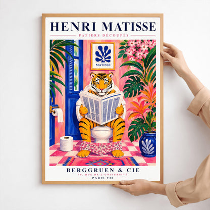 A vertical art print styled as a Henri Matisse exhibition poster. In the center, a tiger sits on a toilet in a pink bathroom, reading a newspaper with pink floral pants at its ankles. The room is decorated with lush tropical plants, a blue door, and a small Matisse-style blue cutout art piece on the wall. The text "HENRI MATISSE" is at the top, and "BERGGRUEN & CIE" is at the bottom.
