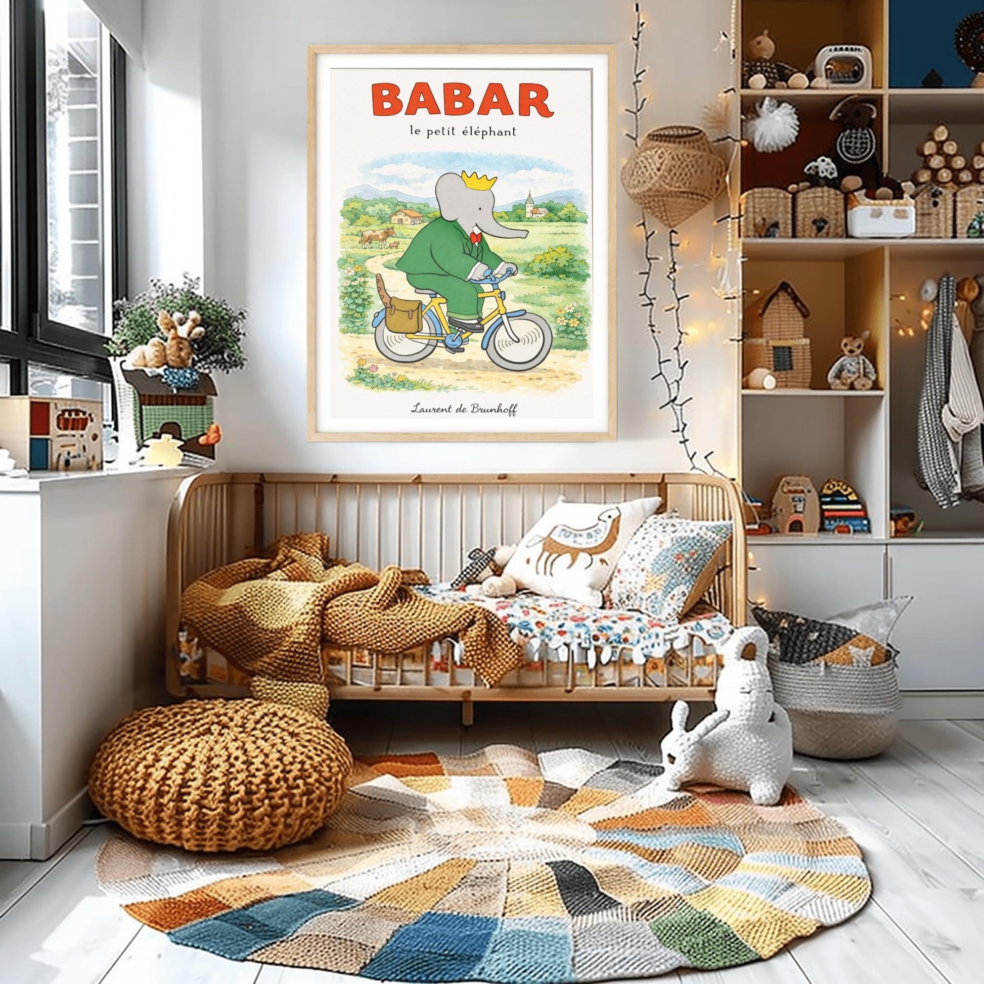 A vertical children's illustration poster titled "BABAR le petit éléphant" at the top in red. King Babar, in a green suit and crown, is riding a yellow bicycle along a dirt path. A brown leather bag on the back of the bike holds a baguette. The background shows a green meadow with a cow and calf, small bushes with flowers, and a distant house and church under a soft sky. The name "Laurent de Brunhoff" is at the bottom.