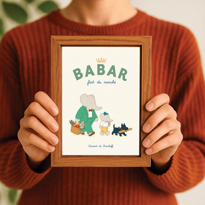 A vertical storybook-style art print of Babar the Elephant walking home from a market against a cream background. Babar is in a green suit and red bow tie, carrying a basket of fruit and flowers. Beside him is a smaller elephant eating an ice cream cone and a small black dog in a plaid collar carrying a baguette. The top text reads "BABAR fait du marché" with a gold crown.