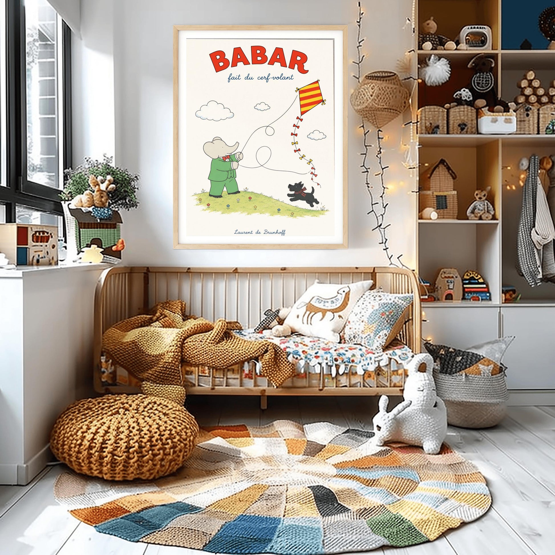 A vertical retro fine art exhibition poster titled "BABAR fait du cerf-volant" on a wide cream border. The top "BABAR" text is printed in a bold red font. The illustration shows an elephant in a green suit and red bowtie flying a red and yellow striped diamond kite on a green grassy hill with small flowers. A small black dog in a plaid scarf runs on the hill below, and the name "Laurent de Brunhoff" anchors the bottom.