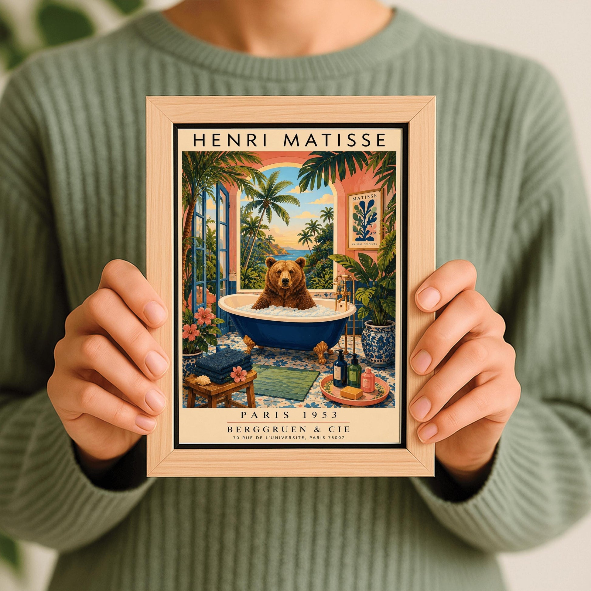 A vertical retro Henri Matisse exhibition poster on a wide cream border. The main image shows a surreal illustration of a large brown bear taking a bubble bath in a navy blue clawfoot tub with gold feet. The bathroom features blue patterned floor tiles, a pink wall with a framed Matisse cut-out poster, and a massive open arch window overlooking a tropical beach with palm trees and a blue ocean at sunset