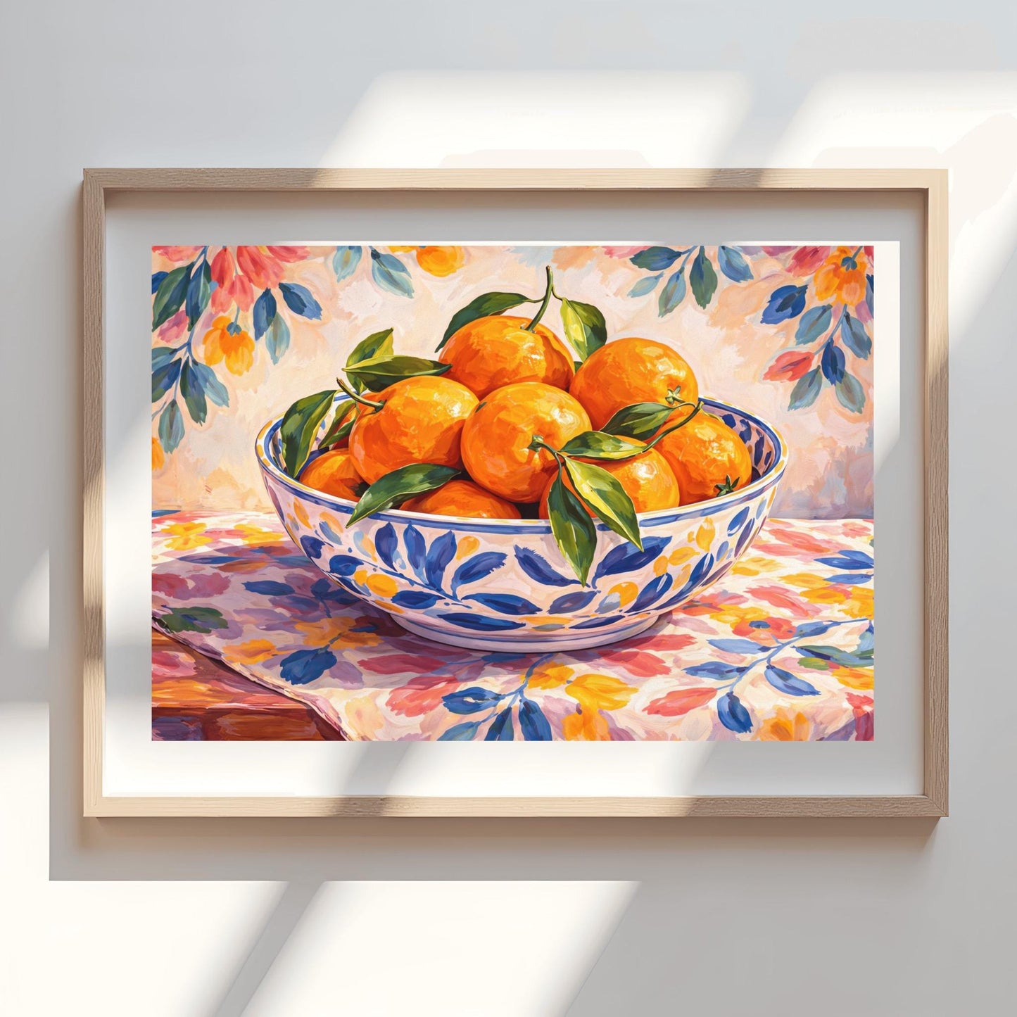 A horizontal painterly illustration of a large blue and white patterned ceramic bowl filled with bright oranges and green leaves. The bowl sits on a table covered with a pink and yellow floral cloth, with a matching soft floral pattern in the background.