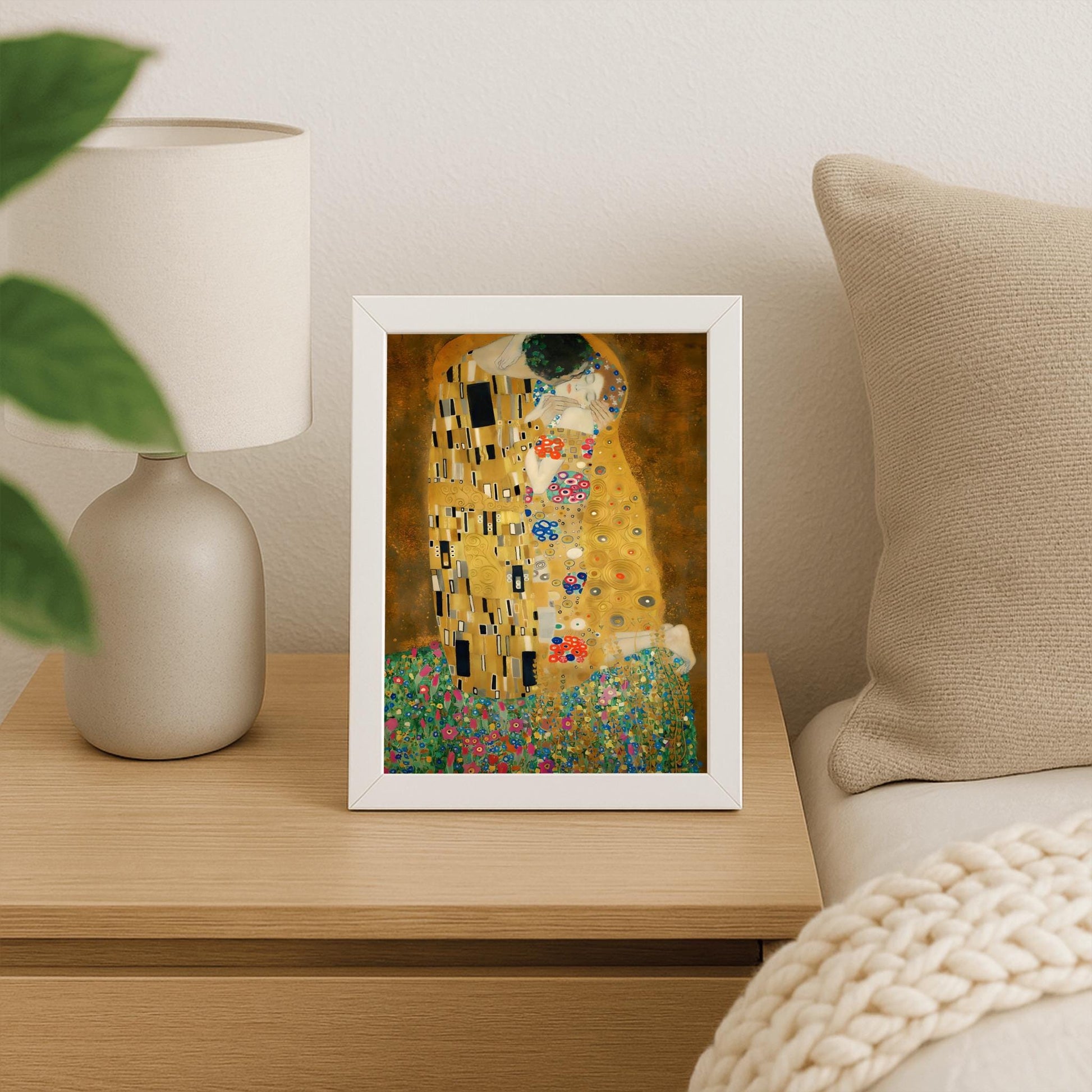 A vertical fine art print of "The Kiss" by Gustav Klimt. Two lovers are shown in an intimate embrace, their bodies covered in elaborate, decorative gold robes. The man's robe features black and white geometric shapes, while the woman's features colorful floral circles. They kneel on a lush bed of colorful wildflowers against a dark, shimmering gold background. The style is rich in mosaic-like patterns and Art Nouveau ornamentation.