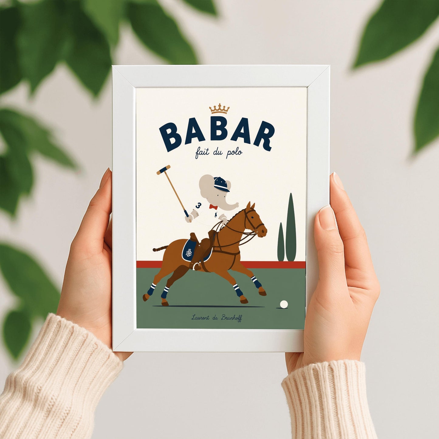 A vertical storybook-style art print of Babar the Elephant playing polo. Babar is riding a chestnut brown horse, wearing a white jersey with the number 3, a red bow tie, and a navy riding helmet. He holds a polo mallet in one hand. The horse has navy and white striped leg wraps. The background features a green field, a red horizon line, and two green cypress trees under a cream sky. The top reads "BABAR fait du polo" with a gold crown.