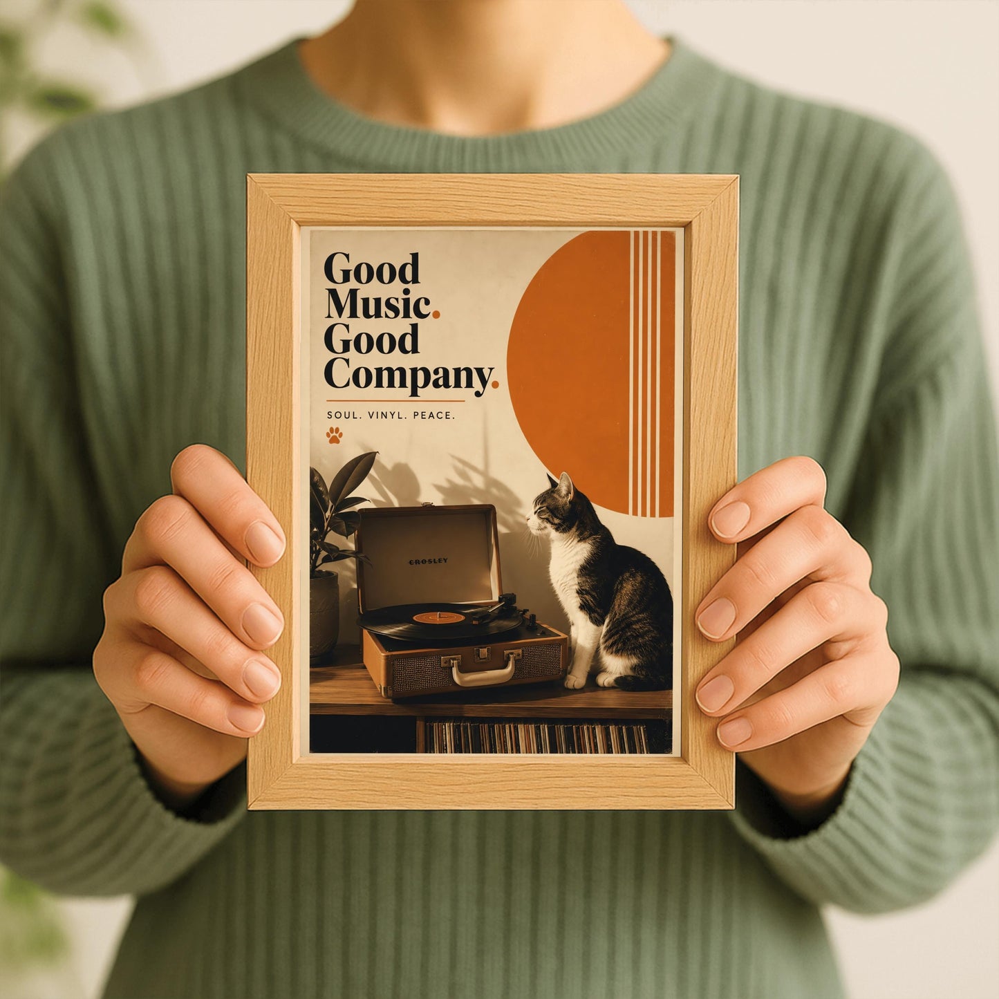A vertical retro fine art poster titled "Good Music. Good Company." on a wide cream border. The design features a bold black serif heading on the left above the text "SOUL. VINYL. PEACE." and a small orange paw print. In the central artwork, a black and white tuxedo cat sits contentedly next to an open tan Crosley record player spinning a vinyl record. A large orange sun shape with white vertical stripes and a potted rubber plant decorate the background.