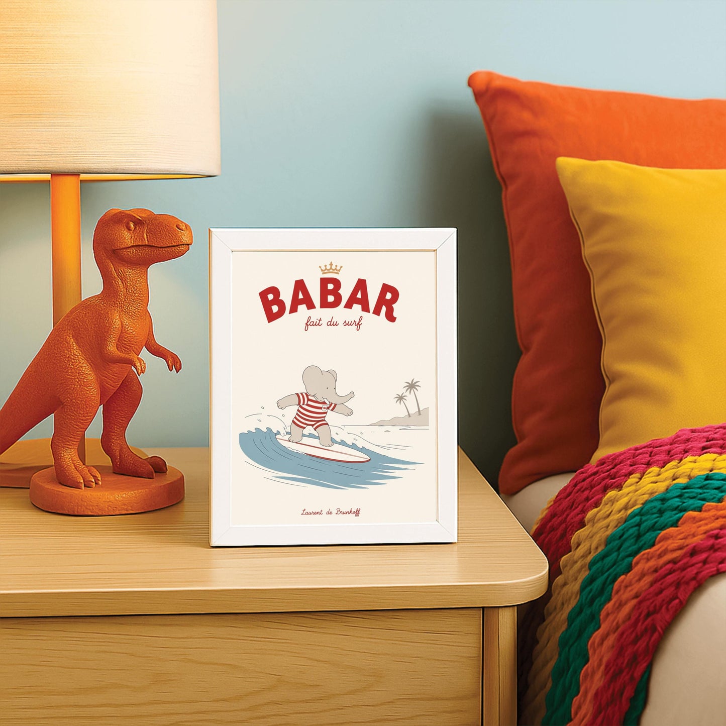 A vertical storybook-style art print of Babar the Elephant surfing. Babar is wearing a red and white striped swimsuit and standing on a white surfboard with a red stripe. He is riding a blue wave with a white crest. In the background, there is a tan beach with two palm trees under a cream sky. The top reads "BABAR fait du surf" with a small gold crown.
