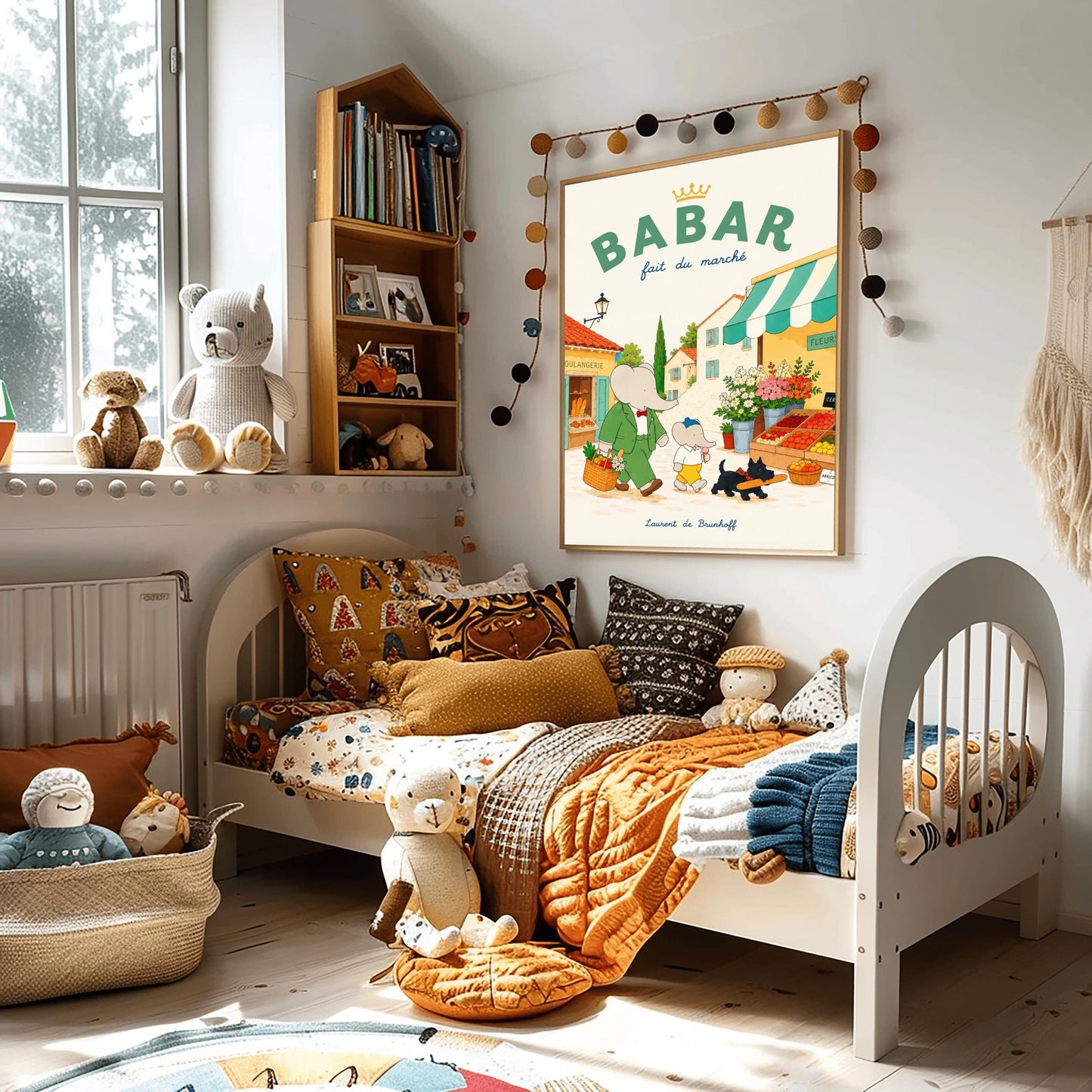 A vertical storybook-style art print of Babar the Elephant walking through a French village street. Babar, in a green suit, carries a basket of groceries. A smaller elephant walks beside him eating a pink ice cream cone, followed by a black dog carrying a baguette. The background features a boulangerie with a yellow facade, a flower stall with pink and white roses, and terracotta-roofed houses under a cream sky. The top reads "BABAR fait du marché" with a gold crown.
