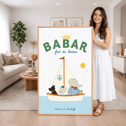A vertical storybook-style art print of Babar the Elephant sailing a boat against a white background. Babar, wearing a blue and white striped shirt and a red neckerchief, sits in a white boat with a smaller elephant and a black dog. The sailboat has a white sail with a blue anchor logo and a red flag on top. A yellow sun and two small birds are in the sky. The top reads "BABAR fait du bateau" with a gold crown.