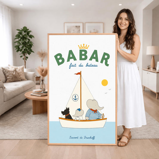 A vertical storybook-style art print of Babar the Elephant sailing a boat against a white background. Babar, wearing a blue and white striped shirt and a red neckerchief, sits in a white boat with a smaller elephant and a black dog. The sailboat has a white sail with a blue anchor logo and a red flag on top. A yellow sun and two small birds are in the sky. The top reads "BABAR fait du bateau" with a gold crown.