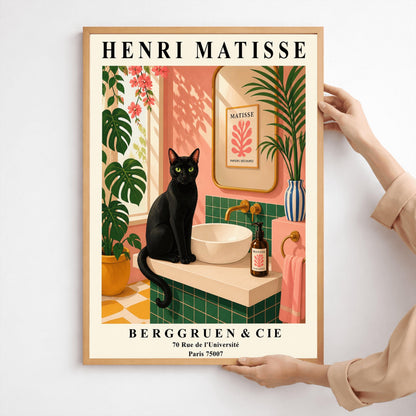 A vertical art print styled as a Henri Matisse exhibition poster. A sleek black cat with bright green eyes sits on a cream-colored bathroom vanity next to a white vessel sink. The bathroom features blush pink walls and emerald green tiles. A gold-framed mirror reflects a Matisse leaf print. Lush green plants and pink flowers frame the scene, and dappled sunlight creates shadows on the wall. The poster has bold black text at the top and bottom with the gallery name Berggruen & Cie.