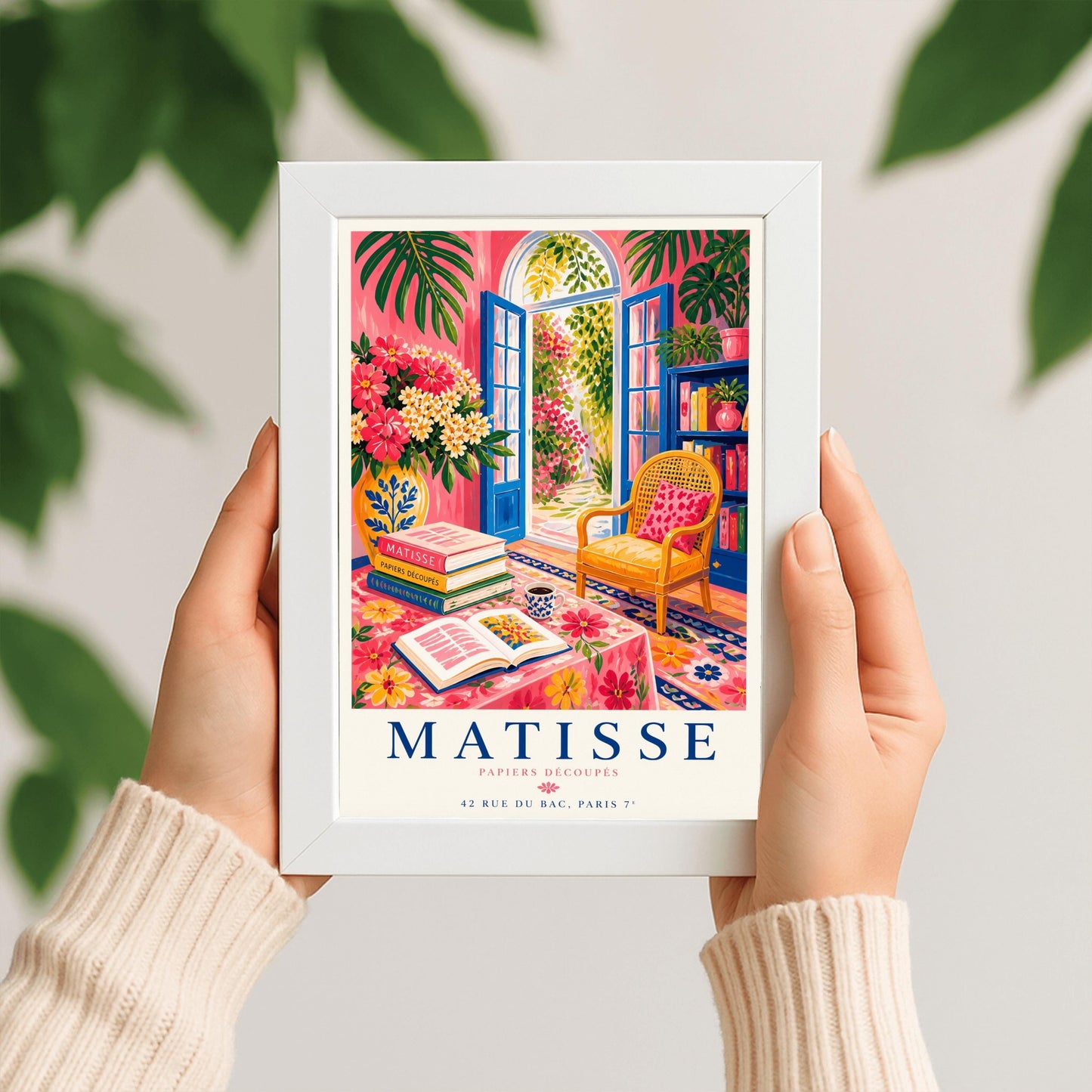 A vertical maximalist art print styled as a Henri Matisse exhibition poster. The scene shows a vibrant interior reading room with hot pink walls and cobalt blue French doors open to a sunlit garden. A yellow cane chair sits next to a bookshelf. In the foreground, a table covered in a pink floral cloth holds a stack of art books, an open book, and a blue coffee mug. Large monstera leaves and various flowers frame the room. Bold black and red text at the bottom reads "MATISSE PAPIERS DÉCOUPÉS"