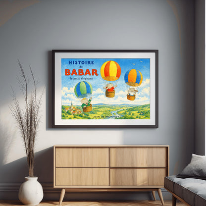 A horizontal watercolor illustration for "Histoire de Babar" showing three elephants in hot air balloons floating over a lush green valley with a river and a small village. On the left, Babar wears a crown and green suit in a blue and green balloon. Two other elephants are in red/orange and blue/yellow balloons. The sky is blue with a few white birds. The title is in large blue and red letters at the top left.