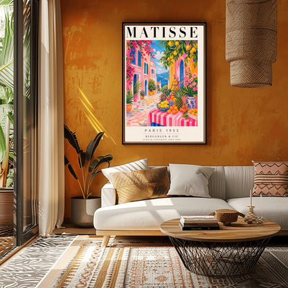 A vertical maximalist art print styled as a Henri Matisse exhibition poster. The scene depicts a vibrant, colorful street in a Mediterranean coastal town. In the foreground, a table with a pink and white striped cloth is piled high with lemons, oranges, and a pineapple. Hot pink and yellow buildings with blue shutters line a cobblestone path that leads toward a blue sea under a bright sky. Lush green trees with yellow lemons and pink flowers frame the view.