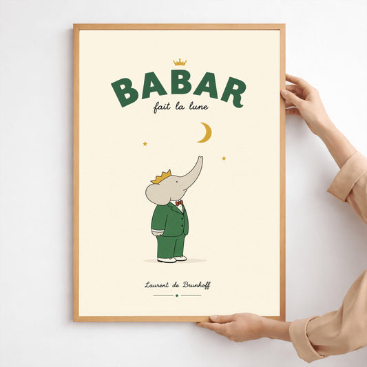 A vertical minimalist children's art print of Babar the Elephant looking up at a crescent moon. Babar is wearing a green suit, a red bowtie, and a golden crown while standing on a light cream background. Above him is a gold crescent moon and two small gold stars. At the top, bold dark green text reads "BABAR" with a gold crown above it and "fait la lune" in script below. The name "Laurent de Brunhoff" is centered at the bottom.