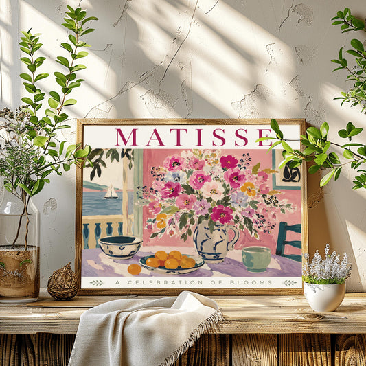 An impressionistic fine art gallery poster titled "MATISSE - A Celebration of Blooms" in elegant magenta lettering. The main painting shows a vibrant indoor still life scene with a textured pastel pink wall. In the center, a white and blue ceramic pitcher overflows with a large bouquet of pink, purple, and yellow flowers. The table is covered in a lavender cloth and holds two patterned bowls filled with orange clementines.