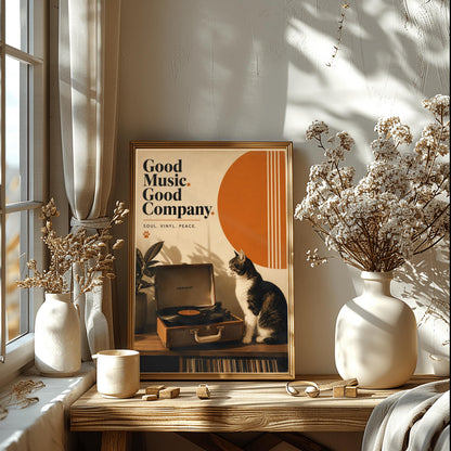A vertical retro fine art poster titled "Good Music. Good Company." on a wide cream border. The design features a bold black serif heading on the left above the text "SOUL. VINYL. PEACE." and a small orange paw print. In the central artwork, a black and white tuxedo cat sits contentedly next to an open tan Crosley record player spinning a vinyl record. A large orange sun shape with white vertical stripes and a potted rubber plant decorate the background.
