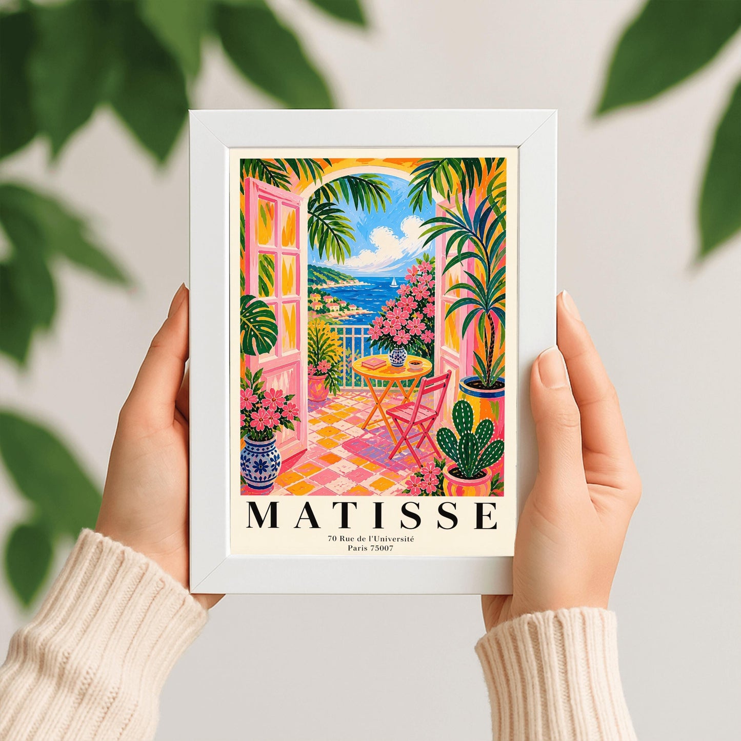 A vertical maximalist art print styled as a Henri Matisse exhibition poster. The scene features a vibrant balcony with pink-framed glass doors open to a view of the blue Mediterranean sea and a coastal town. The balcony has pink and yellow checkered tiles, a yellow round table with a pink chair, and is filled with tropical plants and pink flowers in blue and white vases. A sailboat is visible on the water under a bright blue sky with white clouds.