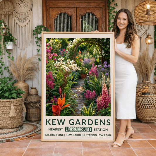 A vertical retro London Underground travel poster for Kew Gardens on a wide cream border. The top image shows a close-up, beautifully detailed illustration of a winding cobblestone garden pathway surrounded by dense flower borders. The foreground features tall pink lupins, a bright orange lily, and clusters of small white flowers. On the right sits a grey wooden bench under purple alliums. The path leads to a wooden archway covered in climbing white roses in the background.