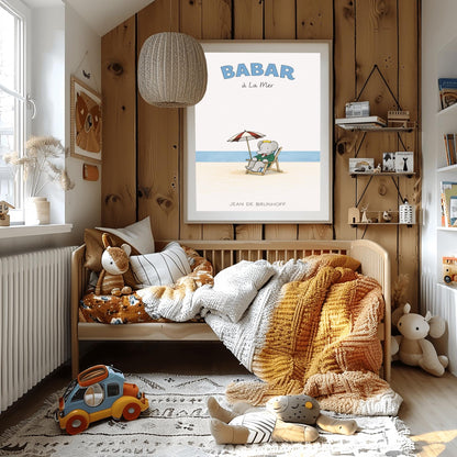 A vertical children's illustration poster titled "BABAR à La Mer" in light blue. In the center, an elephant (Babar) in a green suit and crown is sitting in a wooden lounge chair on a sandy beach. A red and white striped umbrella is behind him. In the background, a thin blue line represents the sea under a white sky. The name "JEAN DE BRUNHOFF" is at the bottom.
