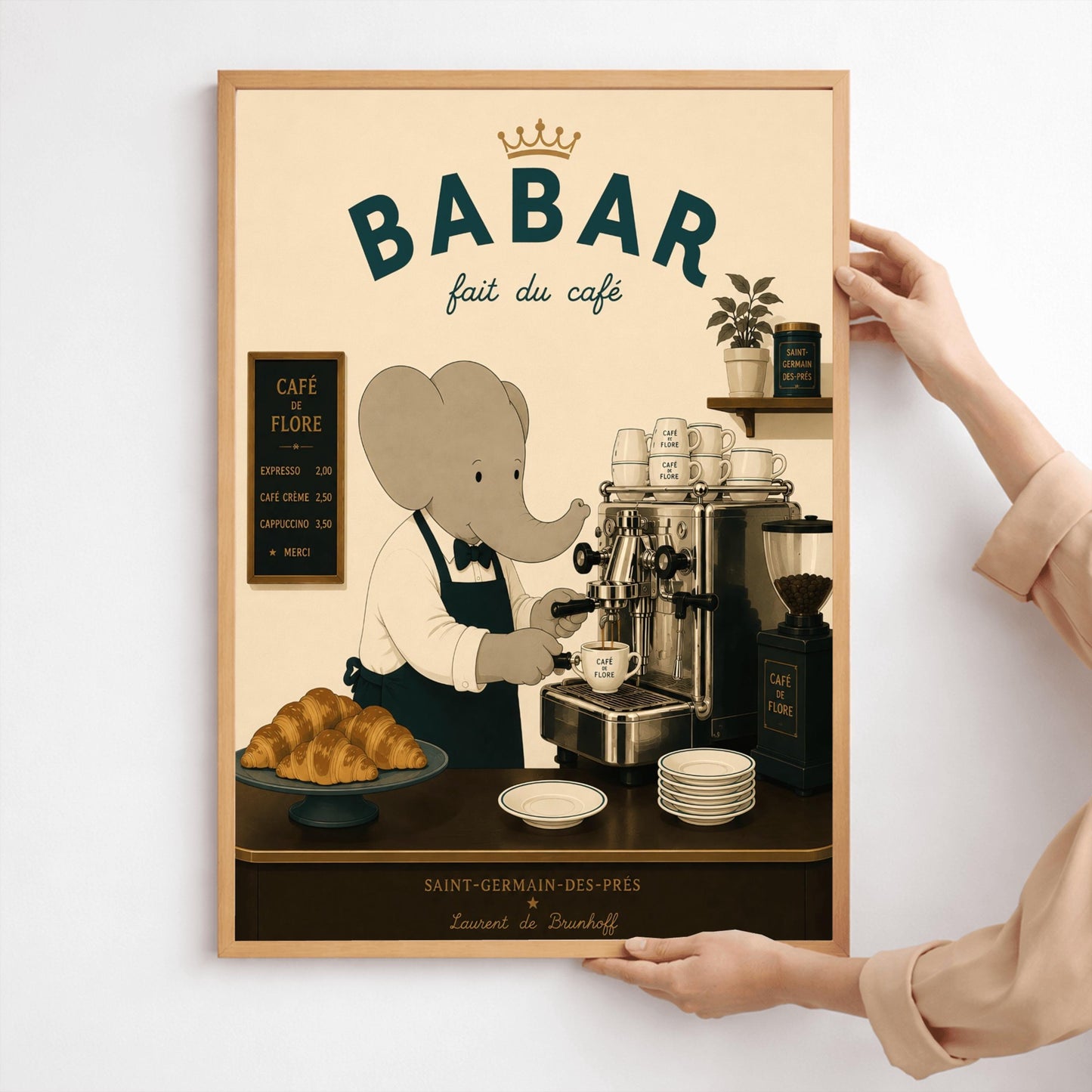 A vintage-style illustration of Babar the Elephant wearing a white shirt, black bowtie, and dark apron, working as a barista. He is operating a classic silver espresso machine in a Parisian café. The scene includes a plate of croissants, stacks of "Café de Flore" cups, and a menu board. The text at the top reads "BABAR fait du café" with a gold crown, and the bottom features "Saint-Germain-des-Prés" and the name "Laurent de Brunhoff."