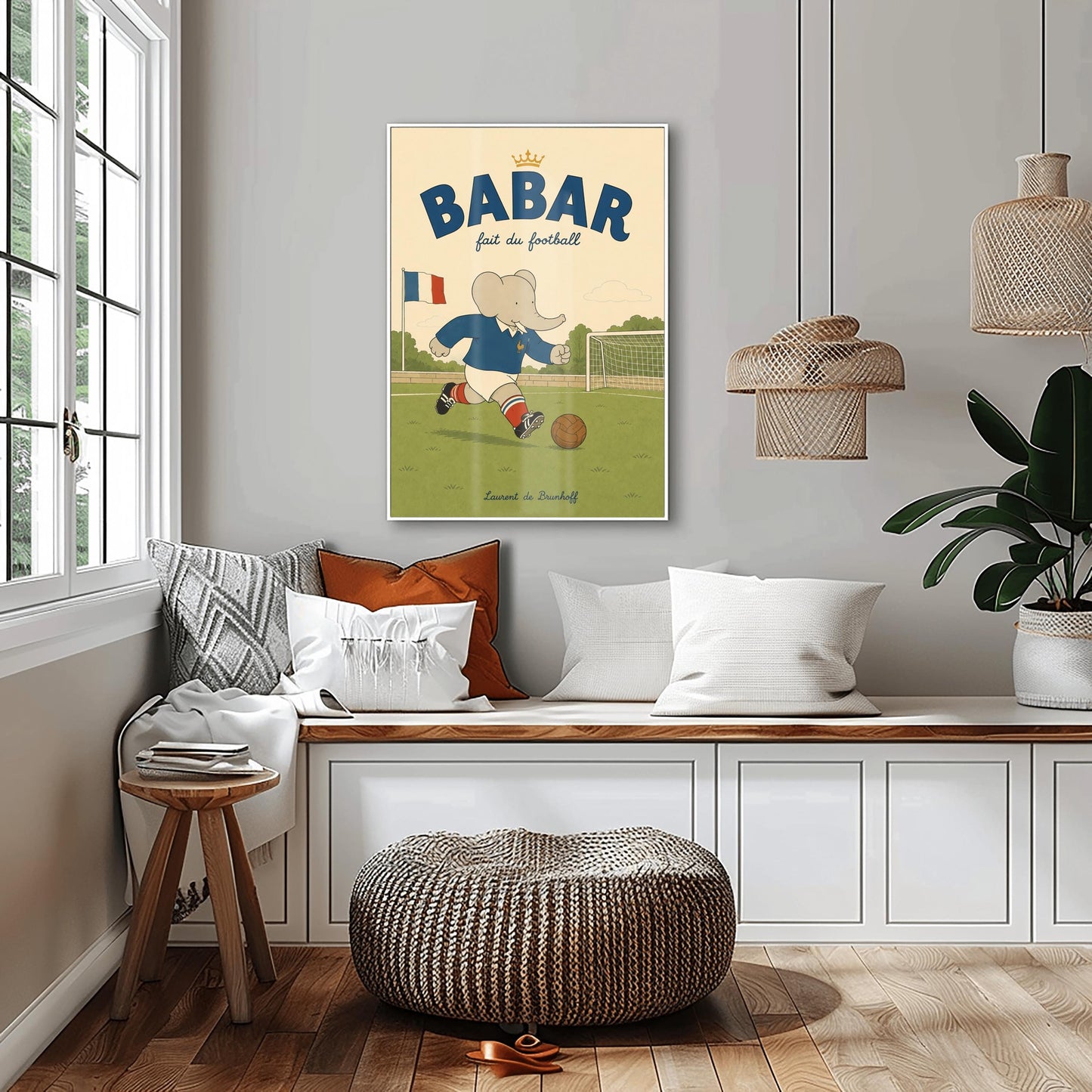 A vertical storybook-style art print featuring Babar the Elephant playing soccer on a green field. Babar wears a blue jersey with a small gold rooster logo, white shorts, red striped socks, and black cleats. He is dribbling a brown leather soccer ball toward a white goal. A French flag flies in the background. The text at the top says "BABAR fait du football" with a small gold crown.