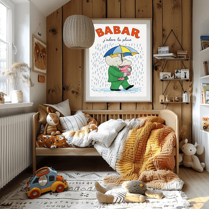 A vertical children's illustration poster titled "BABAR: j'adore la pluie" in orange and blue. King Babar, in a green suit and crown, is walking through the rain while holding a blue and yellow striped umbrella. He is carrying a small elephant wearing a pink rainsuit. They are walking through light blue puddles on a white background. The name "Laurent de Brunhoff" is at the bottom.