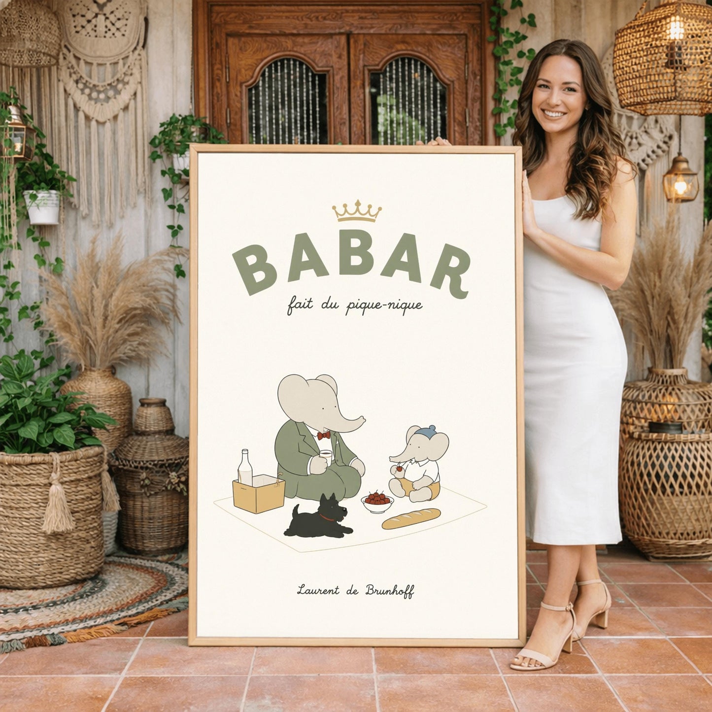 A vertical storybook-style art print of Babar the Elephant having a picnic against a cream background. Babar, in a green suit, sits on a white blanket with a smaller elephant in a blue hat and yellow shorts. A small black dog lies in the foreground. The spread includes a baguette, a bowl of cherries, and a bottle. The top reads "BABAR fait du pique-nique" with a gold crown, and the bottom says "Laurent de Brunhoff."