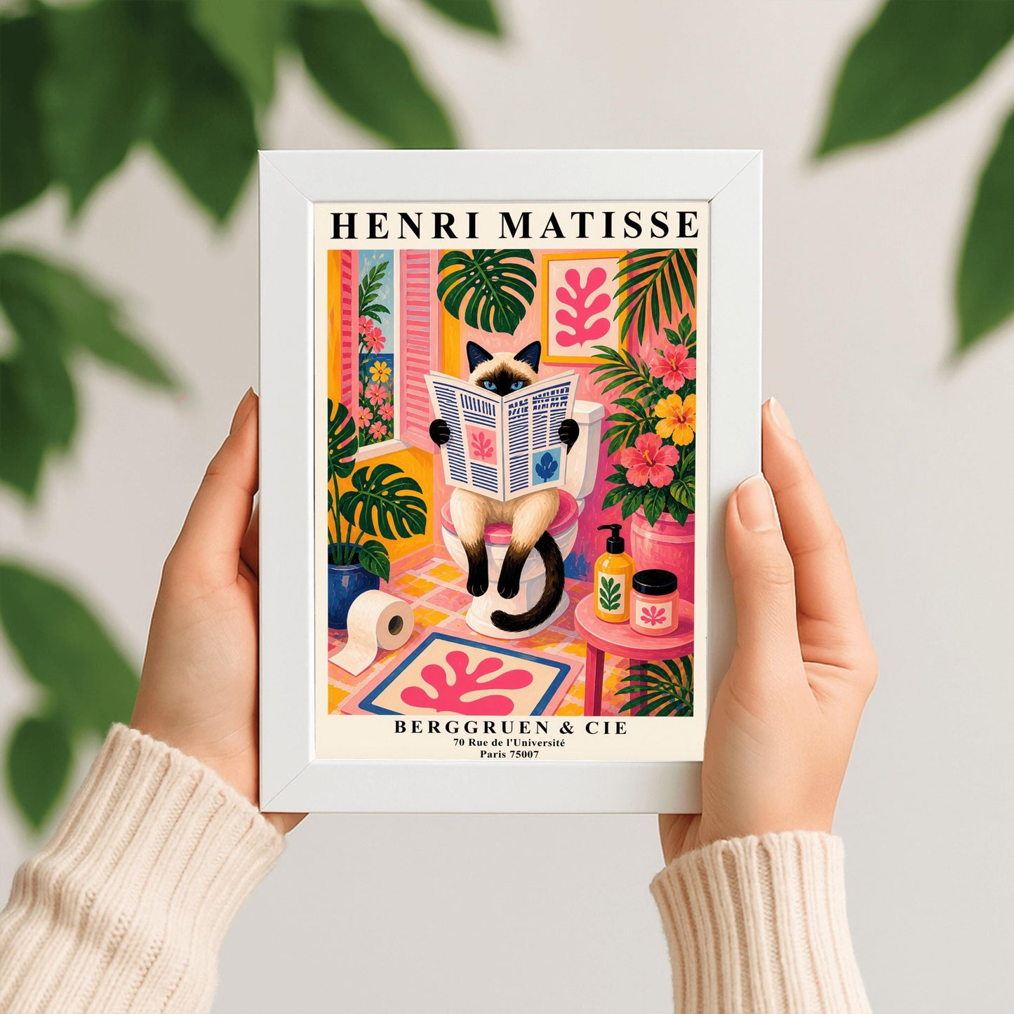 A vertical maximalist art print designed as a Henri Matisse exhibition poster. A cream-colored Siamese cat with dark brown points and blue eyes sits on a toilet, holding and reading a newspaper. The bathroom is vibrantly colored with pink walls, yellow and pink checkered tiles, and lush green monstera plants. A window with pink shutters looks out onto a blue sea. A pink bath mat with a leaf cut-out design and colorful soap jars add to the eclectic decor.