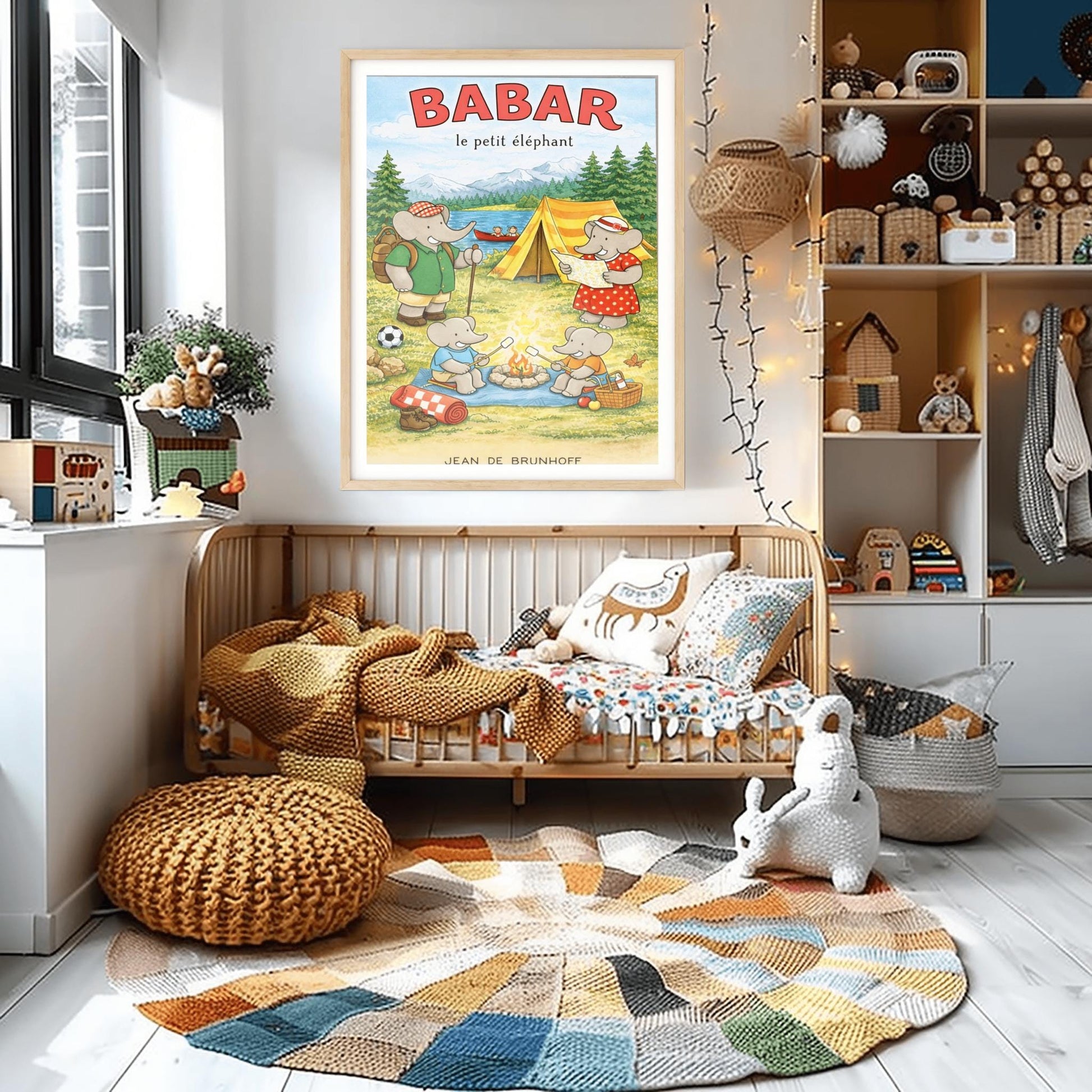 A vertical children's illustration poster titled "BABAR le petit éléphant" at the top in red. It features an elephant family camping by a lake. A large elephant (Babar) in a green shirt stands to the left with a backpack and walking stick. Another large elephant (Celeste) in a red polka-dot dress looks at a map near a yellow tent. Two small elephants sit in the foreground roasting marshmallows over a campfire. The background shows a lake with a red canoe and snow-capped mountains.