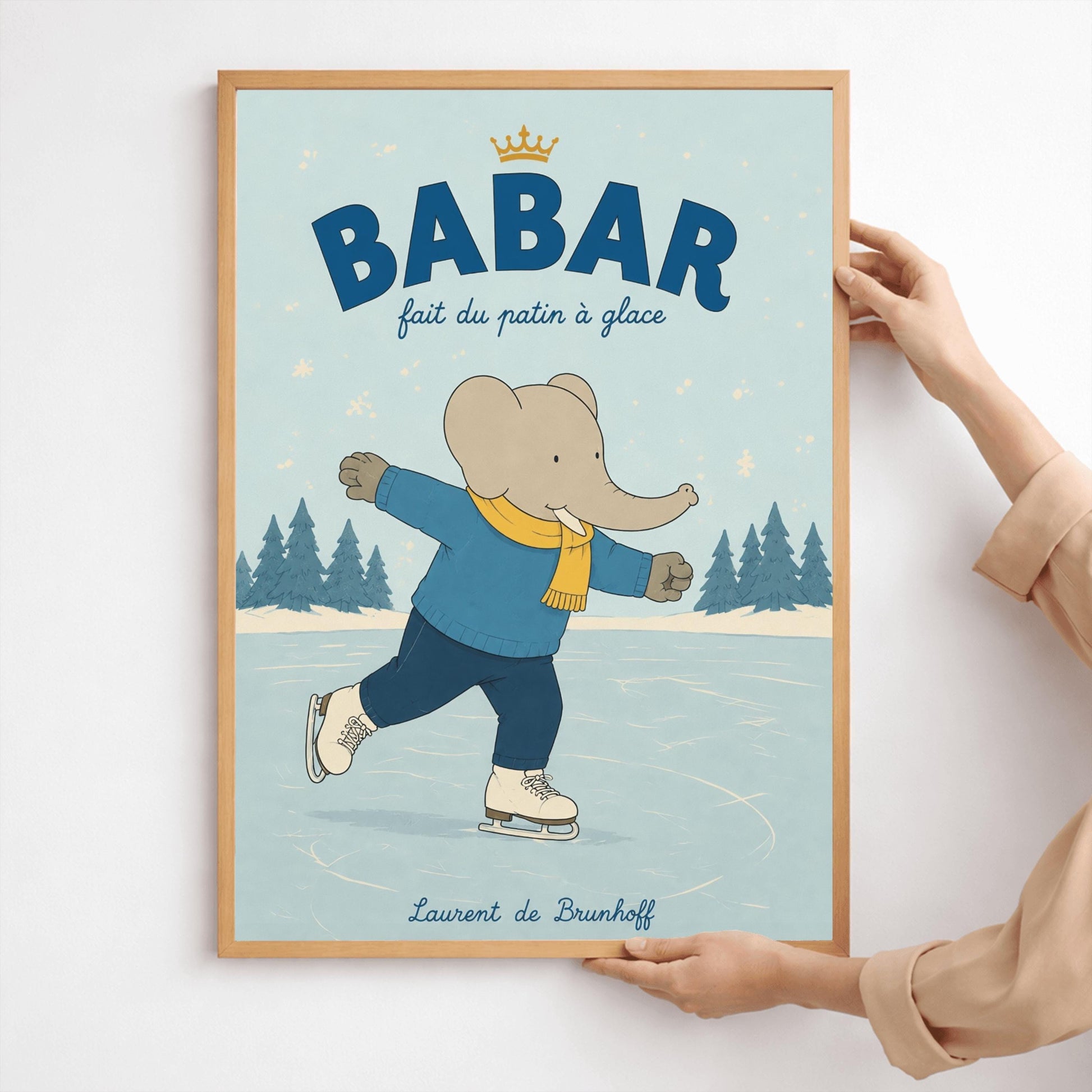 A vertical storybook-style art print featuring Babar the Elephant ice skating on a frozen pond. Babar is wearing a blue sweater, dark pants, a yellow scarf, and white ice skates. He is shown mid-stride with one leg lifted. The background consists of snowy pine trees under a light blue sky with falling snowflakes. The top of the print reads "BABAR fait du patin à glace" with a small gold crown.
