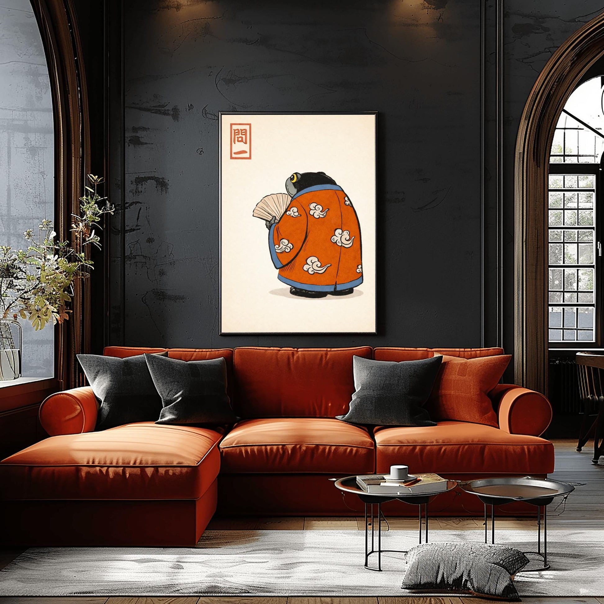 A vertical Japanese woodblock-style art print of a large, dark grey-black frog seen from behind. The frog is wearing an ornate burnt orange kimono decorated with white cloud motifs and blue piping. It holds a beige folding fan in its small hand. In the top left corner is a red rectangular stamp containing Japanese calligraphy. The entire image is set against a textured, pale cream background in a minimalist aesthetic.