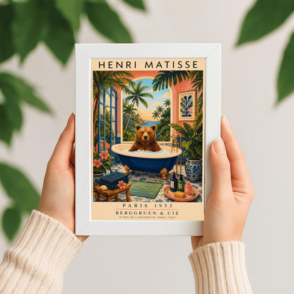 A vertical retro Henri Matisse exhibition poster on a wide cream border. The main image shows a surreal illustration of a large brown bear taking a bubble bath in a navy blue clawfoot tub with gold feet. The bathroom features blue patterned floor tiles, a pink wall with a framed Matisse cut-out poster, and a massive open arch window overlooking a tropical beach with palm trees and a blue ocean at sunset