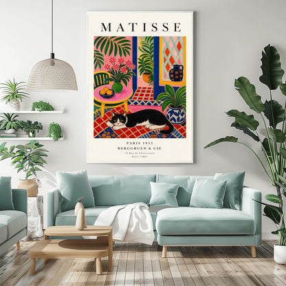A vertical maximalist art print styled as a Henri Matisse exhibition poster. A black and white tuxedo cat lies across an intricate red, orange, and blue patterned rug. The room features textured bubblegum pink walls and a cobalt blue door frame. To the left, a pink table holds a bowl of oranges and a green vase with pink flowers. To the right, a blue and white floral pot holds a green plant. A diamond-patterned window is visible in the background.