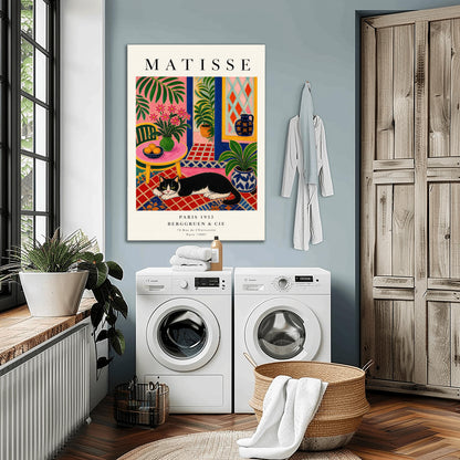 A vertical maximalist art print styled as a Henri Matisse exhibition poster. A black and white tuxedo cat lies across an intricate red, orange, and blue patterned rug. The room features textured bubblegum pink walls and a cobalt blue door frame. To the left, a pink table holds a bowl of oranges and a green vase with pink flowers. To the right, a blue and white floral pot holds a green plant. A diamond-patterned window is visible in the background.