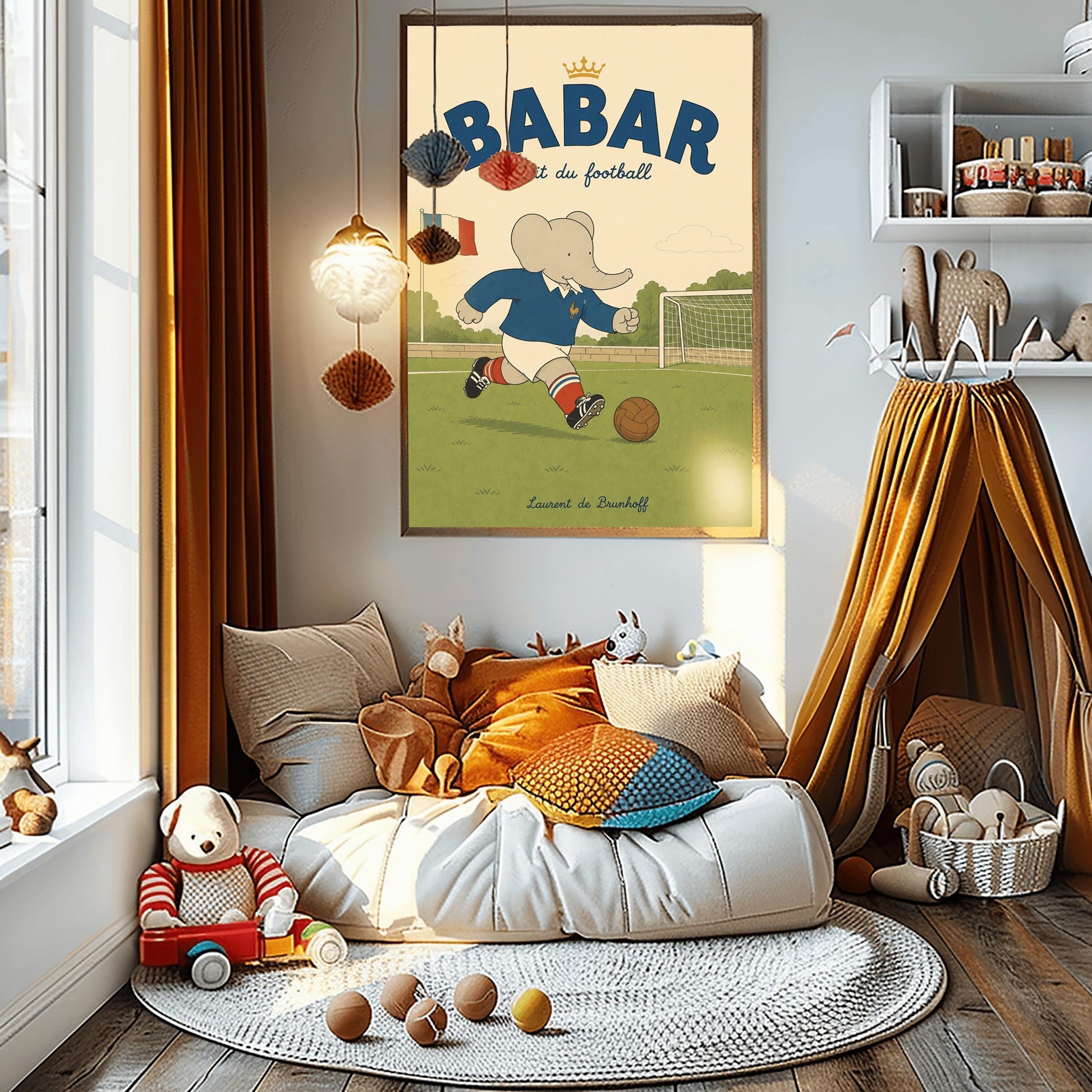 A vertical storybook-style art print featuring Babar the Elephant playing soccer on a green field. Babar wears a blue jersey with a small gold rooster logo, white shorts, red striped socks, and black cleats. He is dribbling a brown leather soccer ball toward a white goal. A French flag flies in the background. The text at the top says "BABAR fait du football" with a small gold crown.