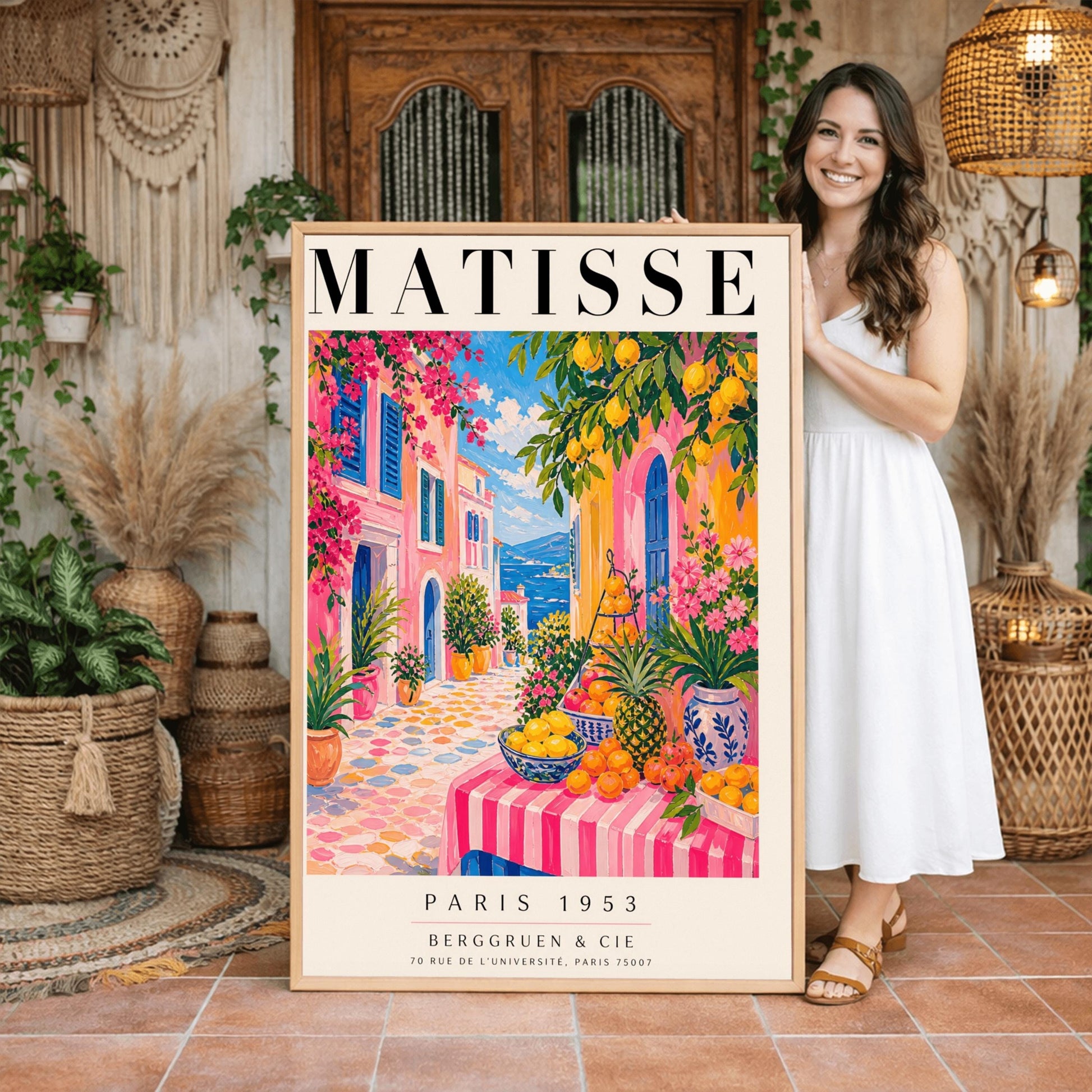 A vertical maximalist art print styled as a Henri Matisse exhibition poster. The scene depicts a vibrant, colorful street in a Mediterranean coastal town. In the foreground, a table with a pink and white striped cloth is piled high with lemons, oranges, and a pineapple. Hot pink and yellow buildings with blue shutters line a cobblestone path that leads toward a blue sea under a bright sky. Lush green trees with yellow lemons and pink flowers frame the view.