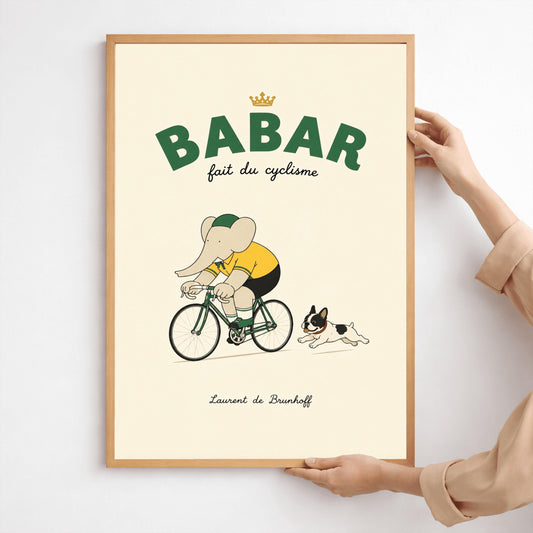 A vertical minimalist children's art print of Babar the Elephant riding a green bicycle. Babar is wearing a yellow shirt and a green-and-yellow cap. A small black-and-white French Bulldog is running playfully behind the bicycle. The background is a solid light cream color. At the top, bold dark green text reads "BABAR" with a gold crown above it and "fait du cyclisme" in script below. The name "Laurent de Brunhoff" is centered at the bottom.