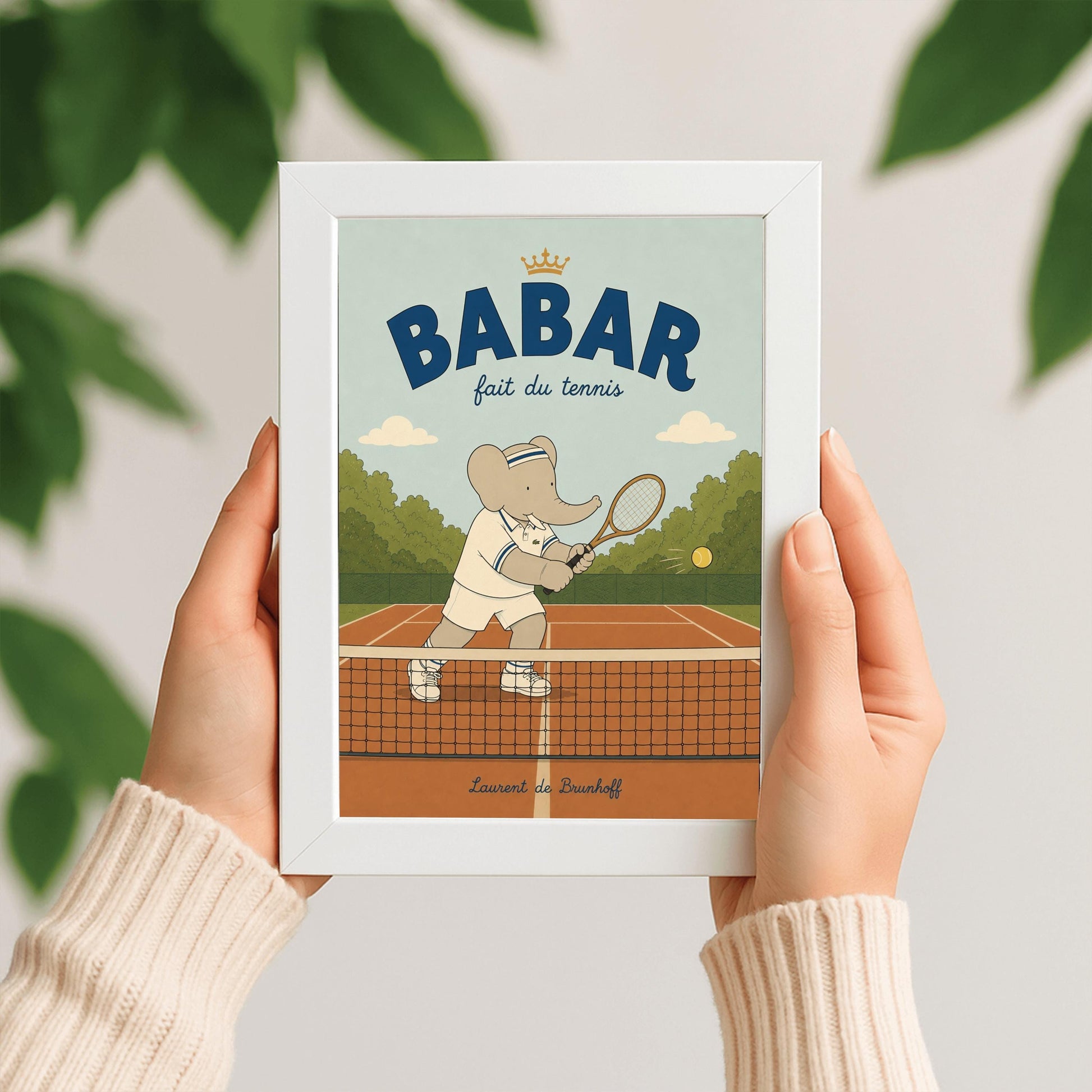 A vertical storybook-style art print featuring Babar the Elephant playing tennis. Babar is seen behind a tennis net on an orange clay court, holding a wooden racket in a backhand swing. He wears a white polo with blue stripes, white shorts, and a blue-and-white striped headband. A yellow tennis ball is in mid-air. The background has green trees and a light blue sky. The top reads "BABAR fait du tennis" with a small gold crown.