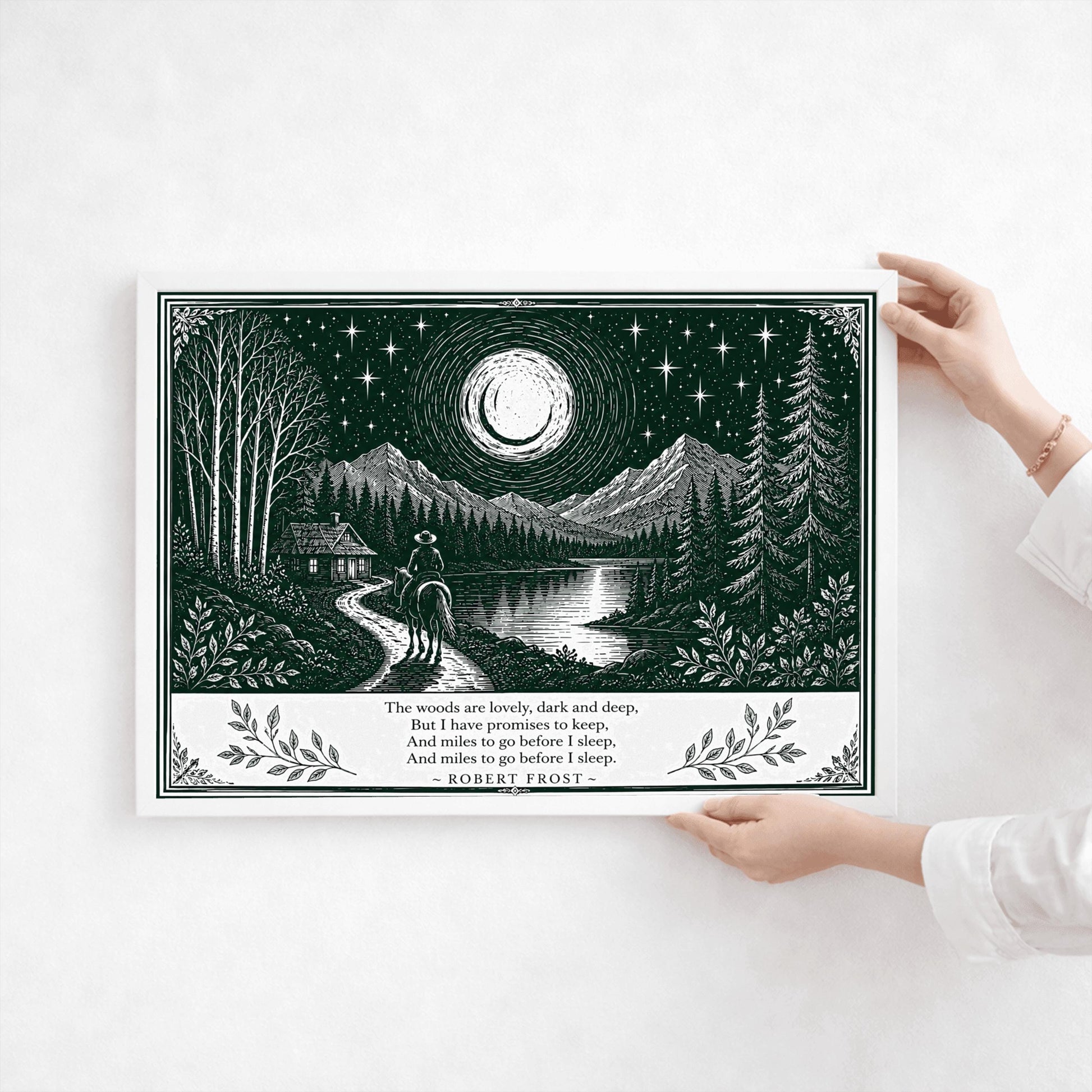 A wide horizontal art print in forest green and cream. A person on horseback follows a path toward a small cabin by a lake. In the background are tall pine forests and sharp mountain peaks under a massive moon and starry sky. The bottom of the print contains four lines of Robert Frost’s poetry in clean serif text, flanked by simple leaf illustrations.