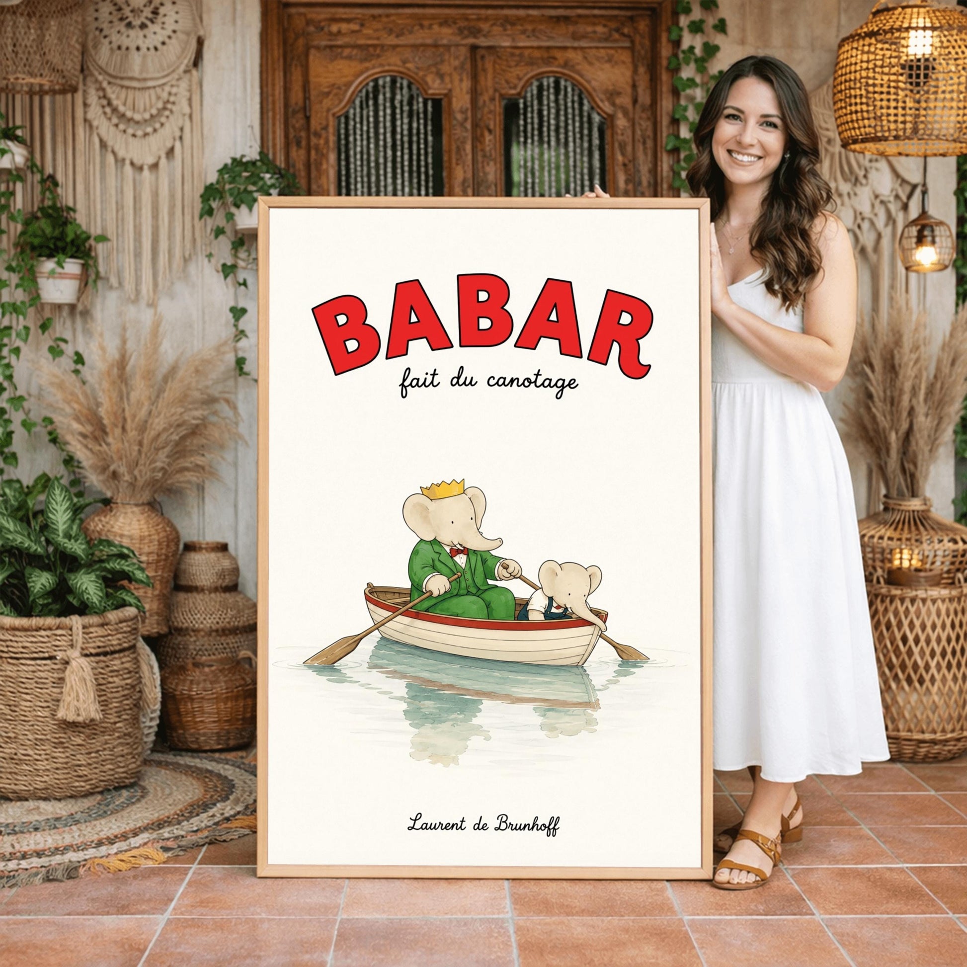 A vertical retro fine art exhibition poster titled "BABAR fait du canotage" on a wide cream border. The top "BABAR" text is printed in a bold red font. The illustration shows an elephant wearing a crown and green suit sitting in a white wooden rowboat with a red rim, holding two oars. A smaller elephant leans over the front of the boat looking at its reflection in the calm water. The name "Laurent de Brunhoff" anchors the bottom.