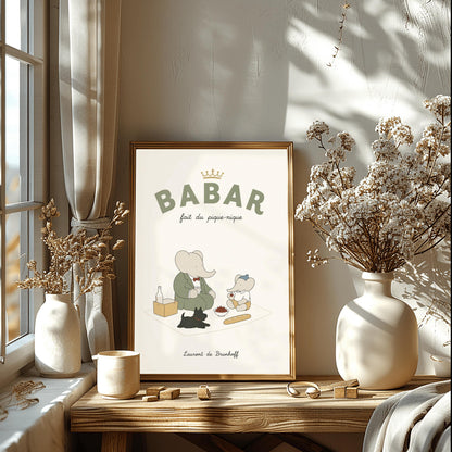 A vertical storybook-style art print of Babar the Elephant having a picnic against a cream background. Babar, in a green suit, sits on a white blanket with a smaller elephant in a blue hat and yellow shorts. A small black dog lies in the foreground. The spread includes a baguette, a bowl of cherries, and a bottle. The top reads "BABAR fait du pique-nique" with a gold crown, and the bottom says "Laurent de Brunhoff."
