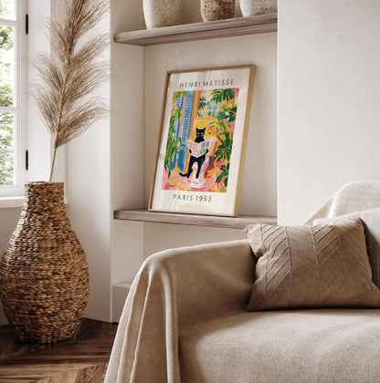 Framed artwork of a cat in a colorful setting on a shelf next to a couch with a pillow.