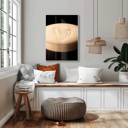 A vertical macro photograph of the thick, creamy foam head on a pint of Guinness. The iconic Guinness harp is embossed into the center of the velvety bubbles. The image features warm cream tones against a dark, shadowy background.